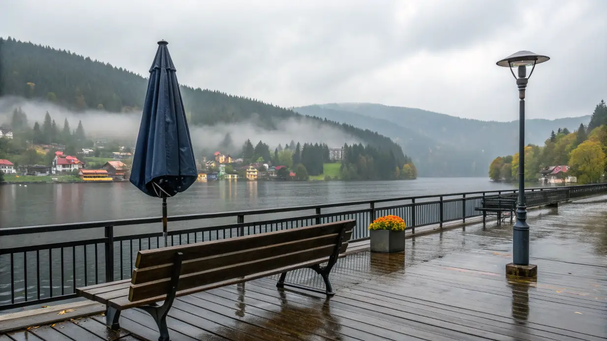Banc vide sur une jetée mouillée à Titisee, avec parapluie fermé, sous une pluie fine, face au lac et aux collines brumeuses de la Forêt-Noire.
